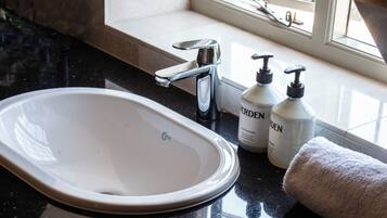 A bathroom with a white sink, a faucet, two bottles of hand sanitizer, and a towel.