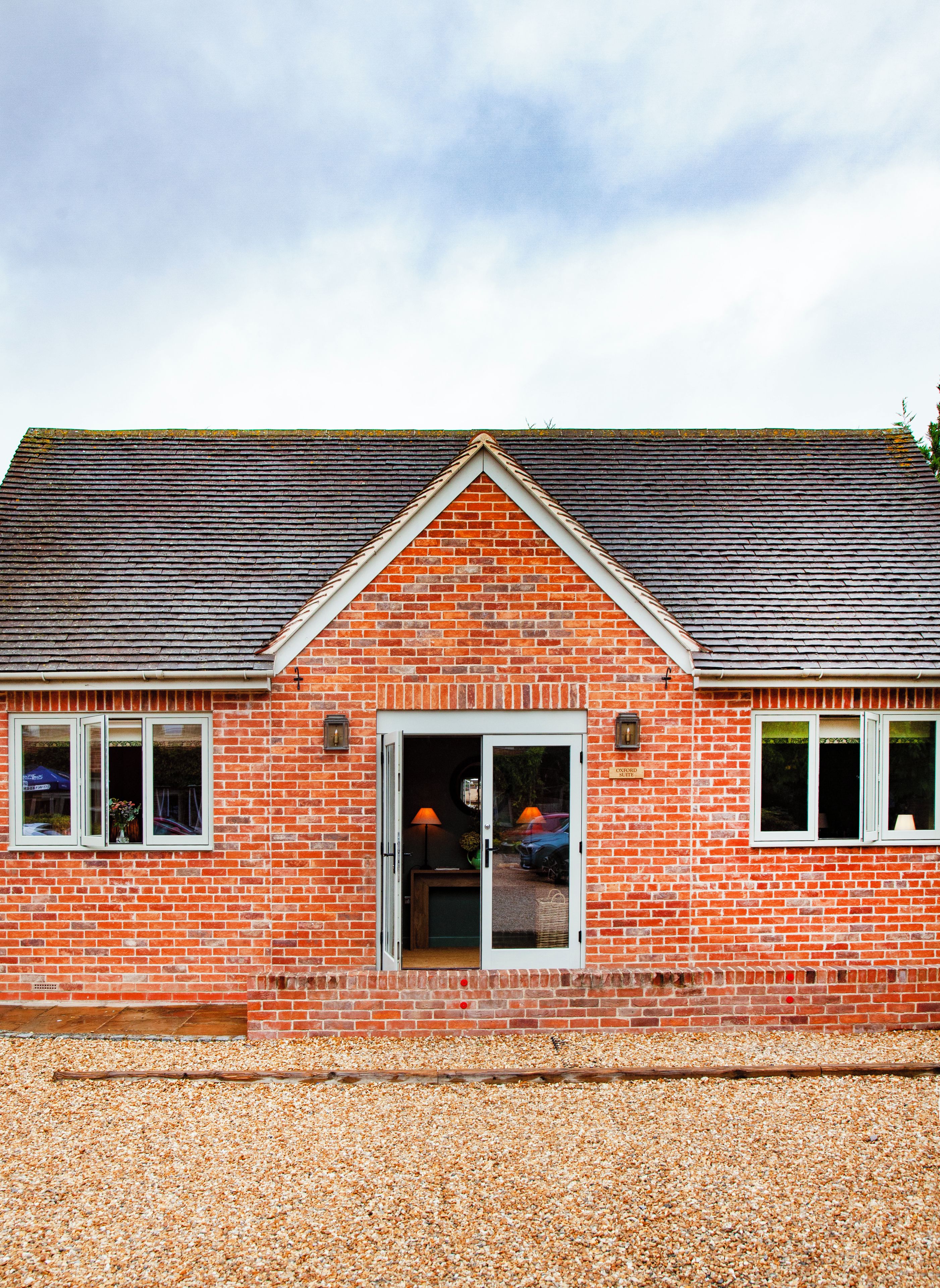 A red brick building with a gabled roof, a front door, and two windows on either side.
