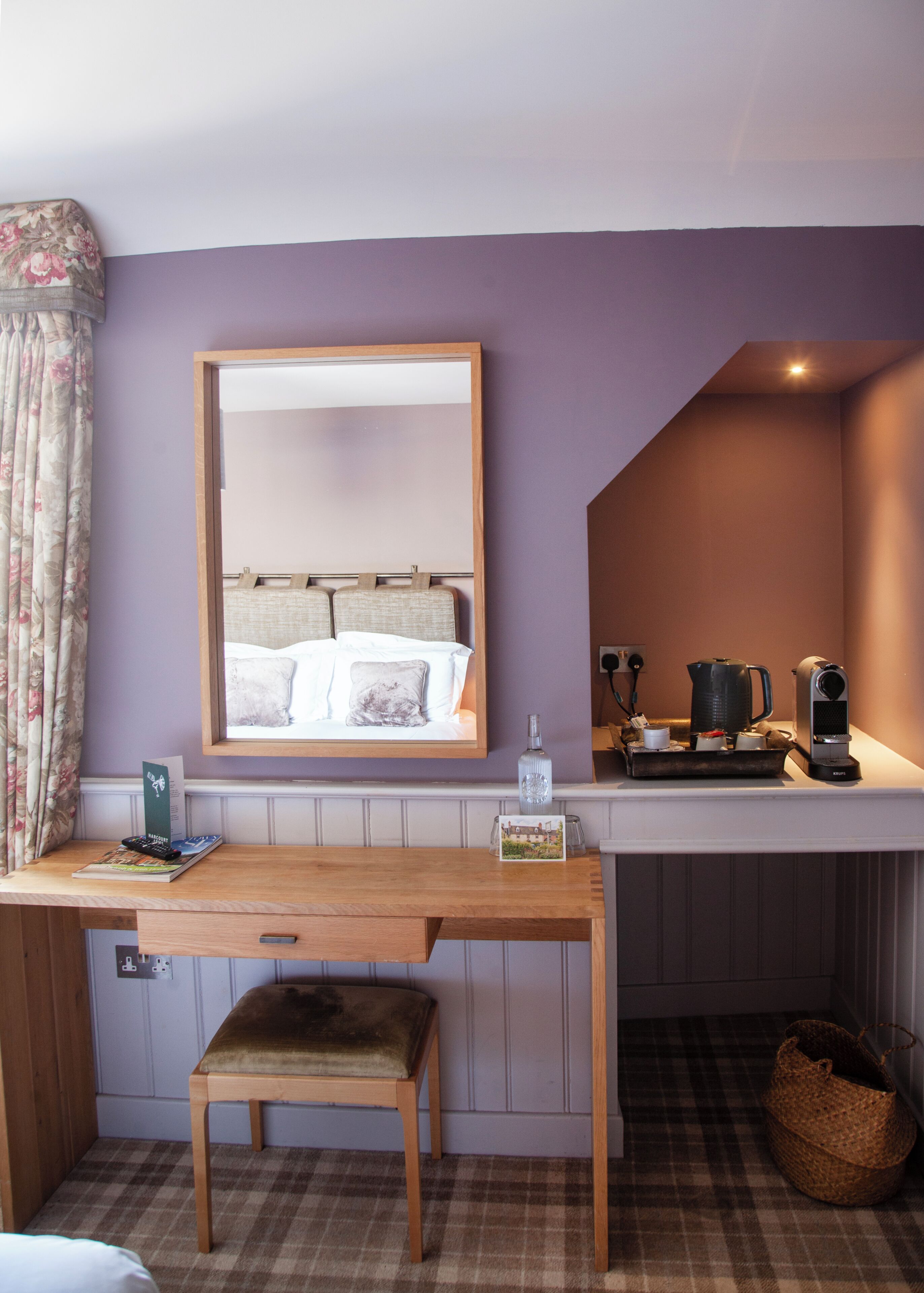 A room with a wooden desk, a mirror, a bed, a small bench, a coffee maker, and a kettle.