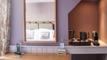 Una habitación con escritorio de madera, un espejo, una cama, un pequeño banco, una cafetera y un hervidor.