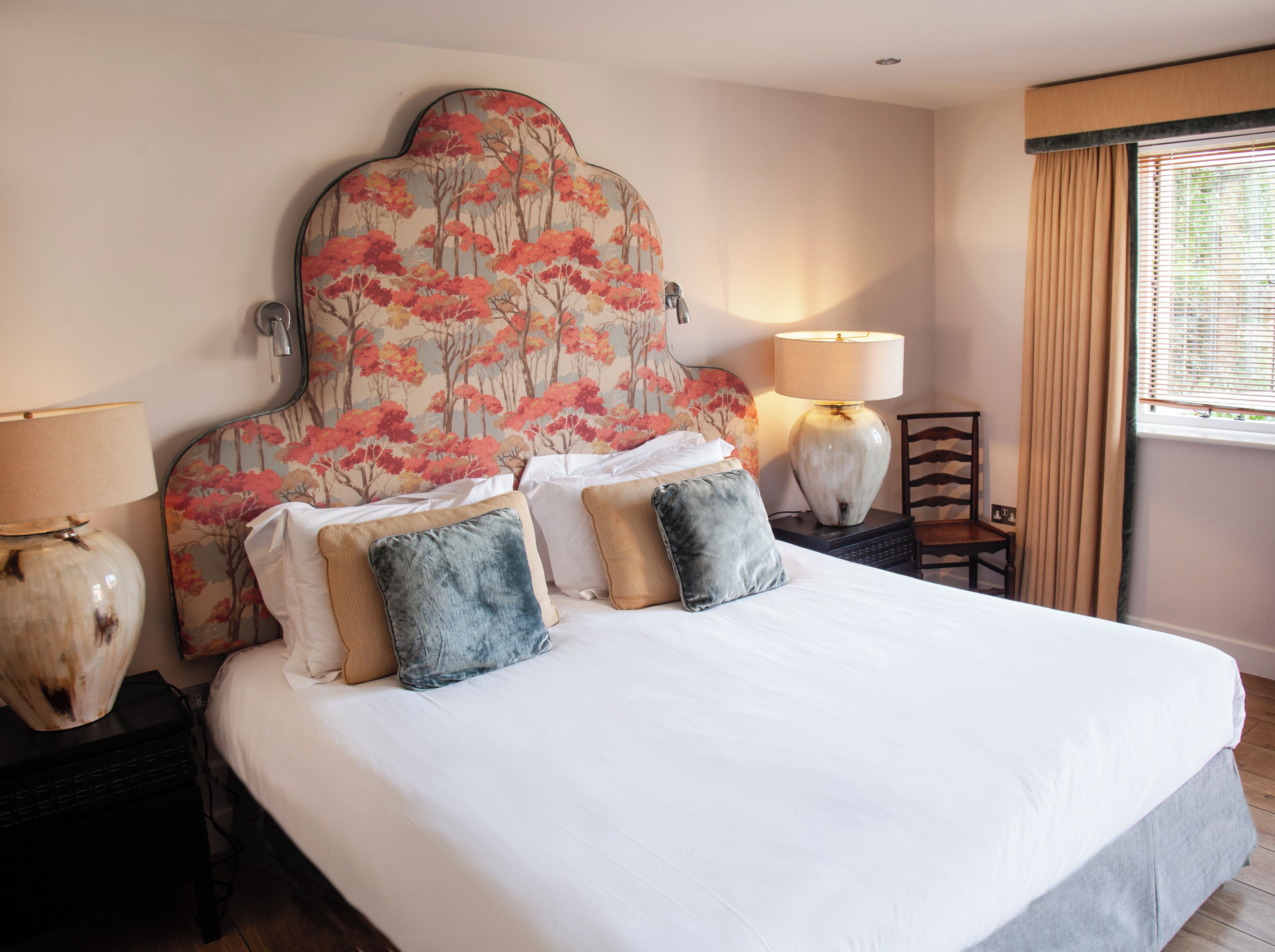 Une chambre d’hôtel avec un grand lit, deux lampes de chevet, une chaise et une fenêtre avec des rideaux.