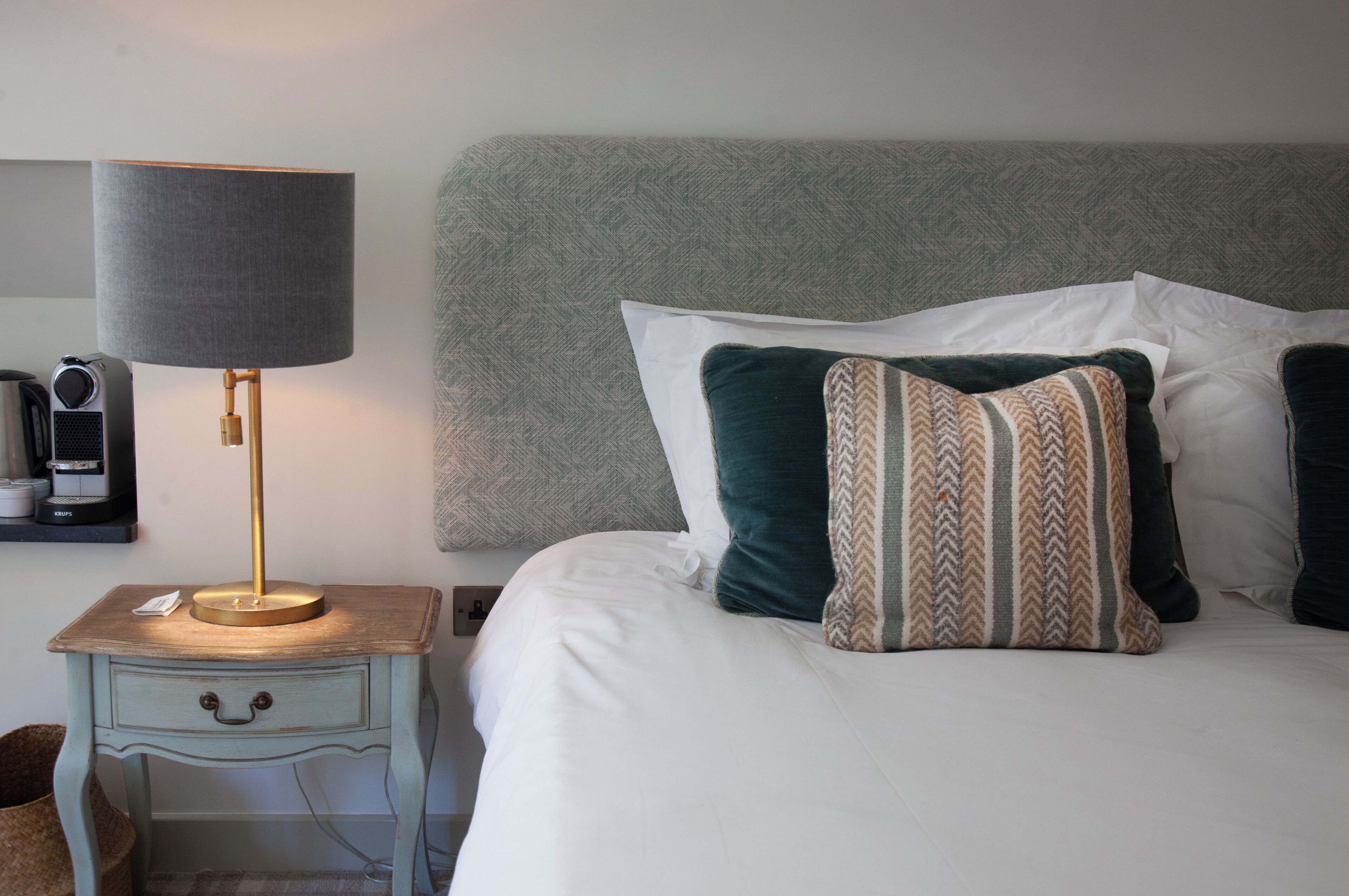 A neatly made bed with white linens, a grey headboard, and decorative pillows.