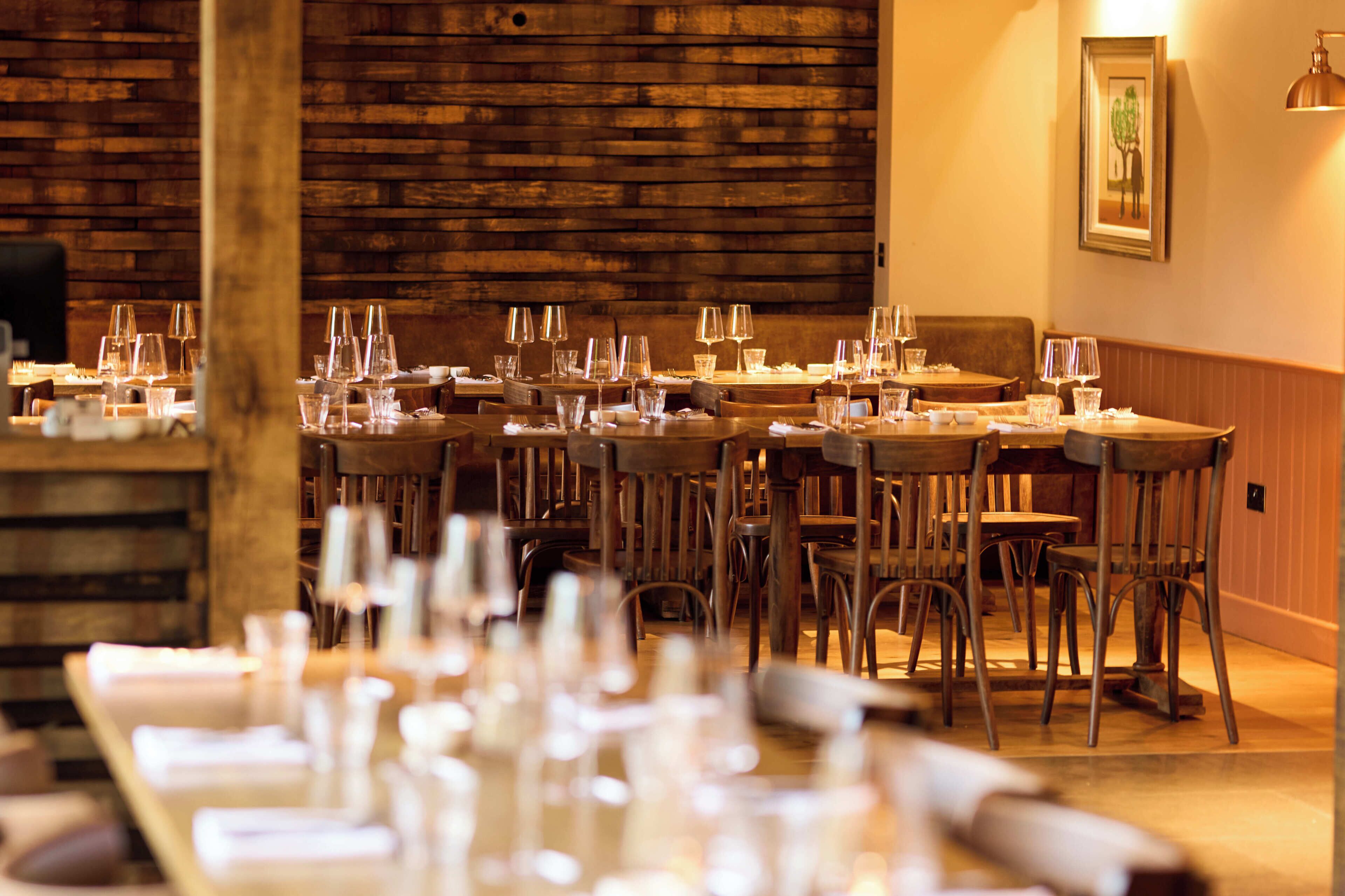 A restaurant with wooden walls, multiple tables set with glasses and cutlery, and a framed picture on the wall.