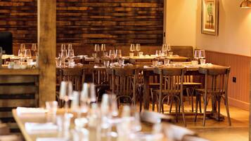 A restaurant with wooden walls, multiple tables set with glasses and cutlery, and a framed picture on the wall.