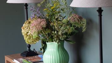 Een houten console tafel met een groene vaas vol bloemen, twee lampen en een stapel boeken.