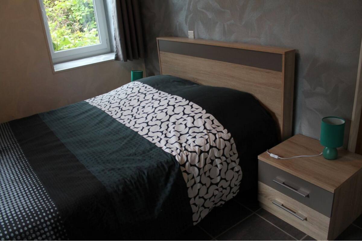 A bedroom with a bed, a bedside table with a lamp, and a window with curtains.