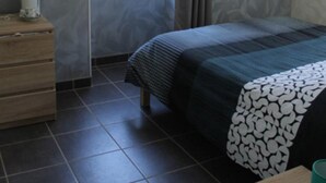Ein Schlafzimmer mit Bett, Kommode, einem Fenster mit Vorhängen und einem kleinen Tisch mit einer Tasse.