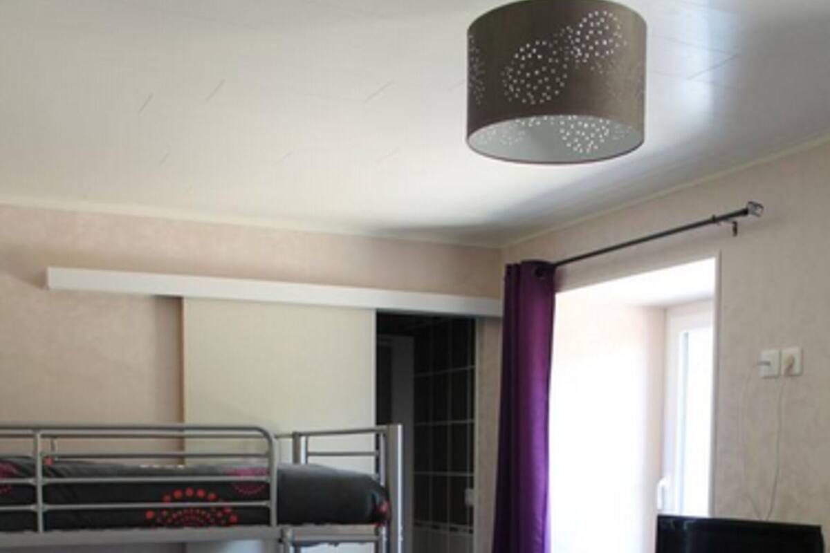 A dormitory room with bunk beds, a television, and a window with curtains.