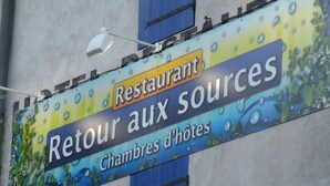 Schild für ein Restaurant namens 'Retour aux sources' mit blau-gelber Farbgebung und Wassertropfen-Grafiken.