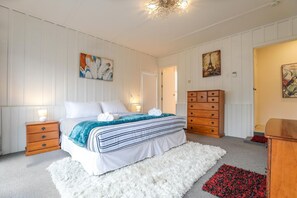 A bedroom with a bed, nightstands, a dresser, and artwork on the walls. - Groovy on Grey - Spa Pool, Central, Sleeps 8 (Rotorua)