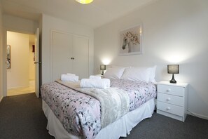 A bedroom with a bed, two bedside tables, a door, and a wall-mounted picture.