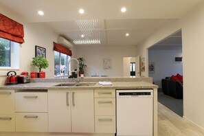 A modern kitchen with a dishwasher, a sink, and a countertop with red kettles. - Groovy on Grey - Spa Pool, Central, Sleeps 8 (Rotorua)