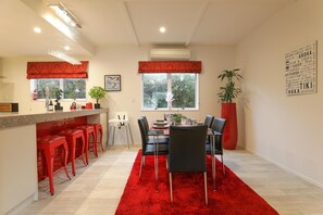 A modern kitchen with a dining area, red accents, and a large window.
