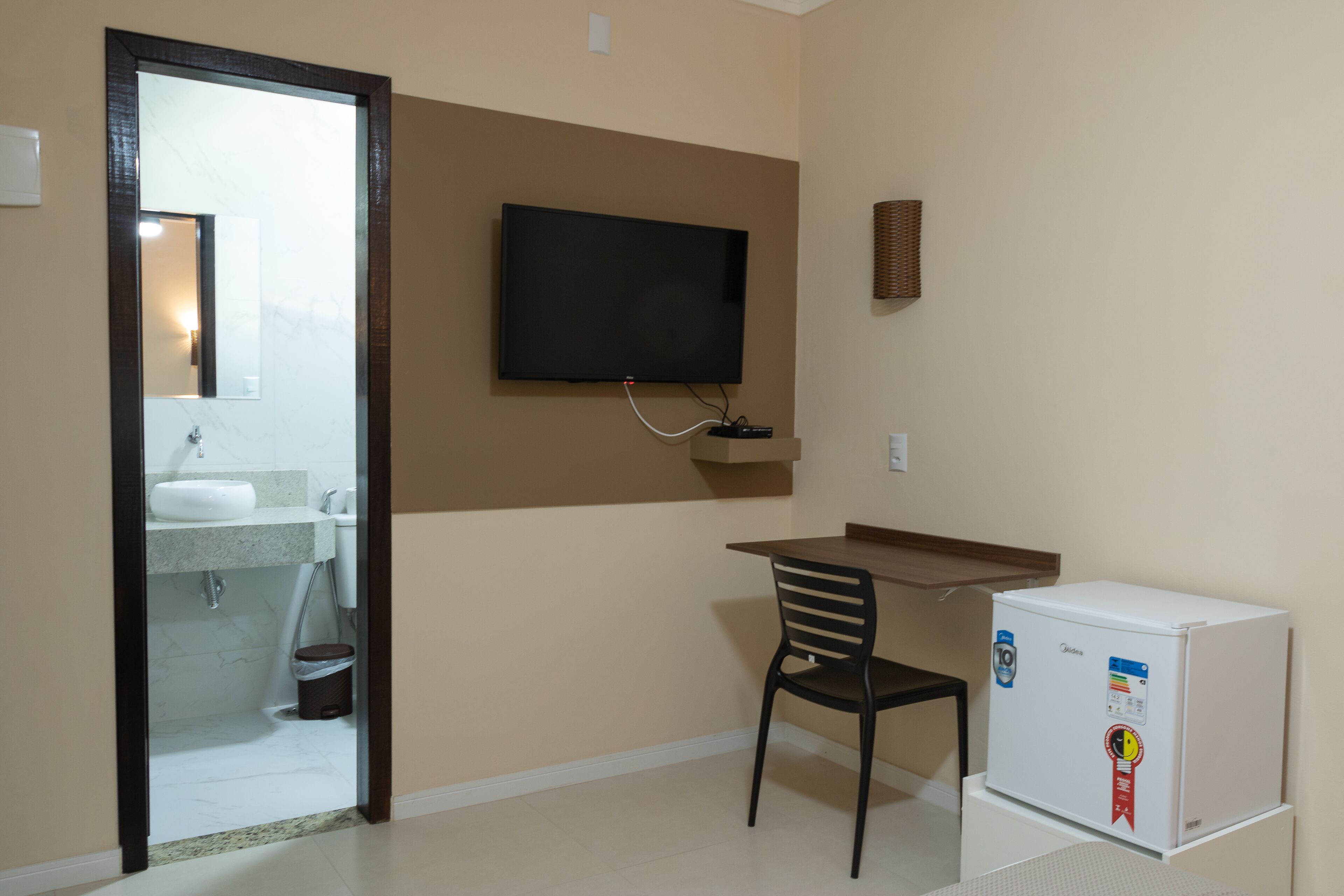 A small room with a desk, chair, television, and a refrigerator.