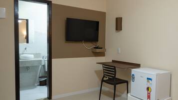 A small room with a desk, chair, television, and a refrigerator.