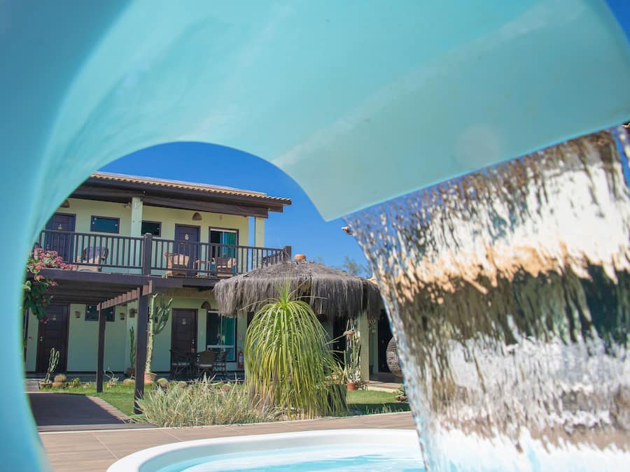 A pool area with a thatched-roof structure, a cactus, and a building with balconies.