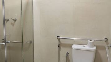 Un baño con cabina de ducha de vidrio, un inodoro con una toalla encima y un pasamanos.
