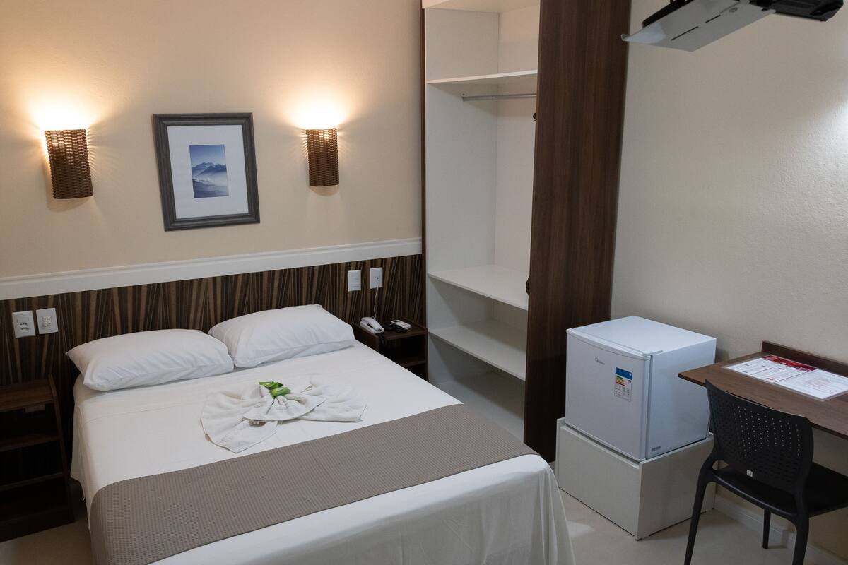 Ein Hotelzimmer mit Bett, Nachttischen, Schreibtisch, Kühlschrank und Wandleuchten.
