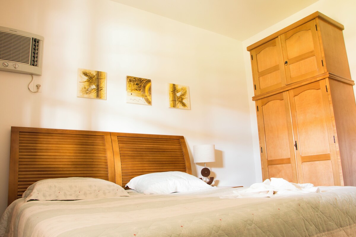Un dormitorio con cabecera de madera, cama con ropa de cama blanca, armario de madera y dos obras de arte colgadas en la pared.