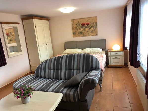 A bedroom with a bed, a nightstand, a dresser, a sofa, and a small table with a flower.