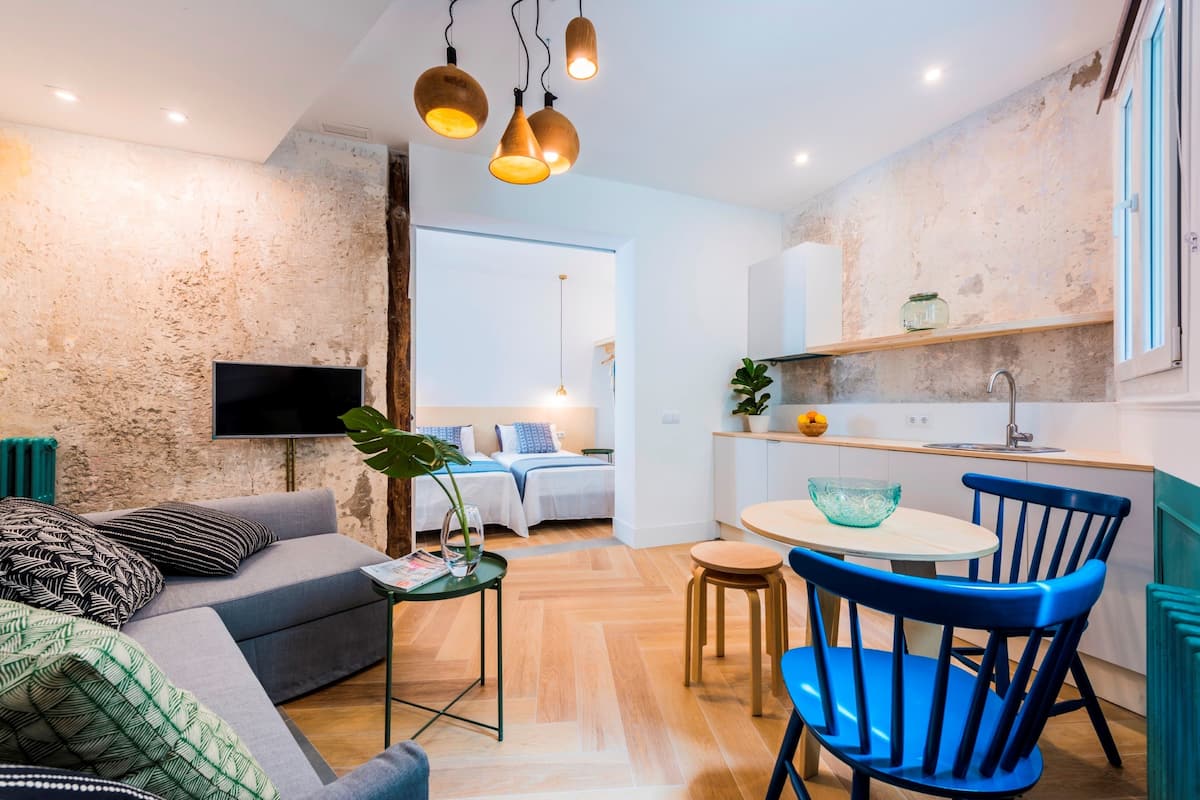 Un espacio habitable compacto con un sofá, una mesa de comedor con sillas, un televisor montado en la pared y una zona de cocina con un fregadero y encimera.