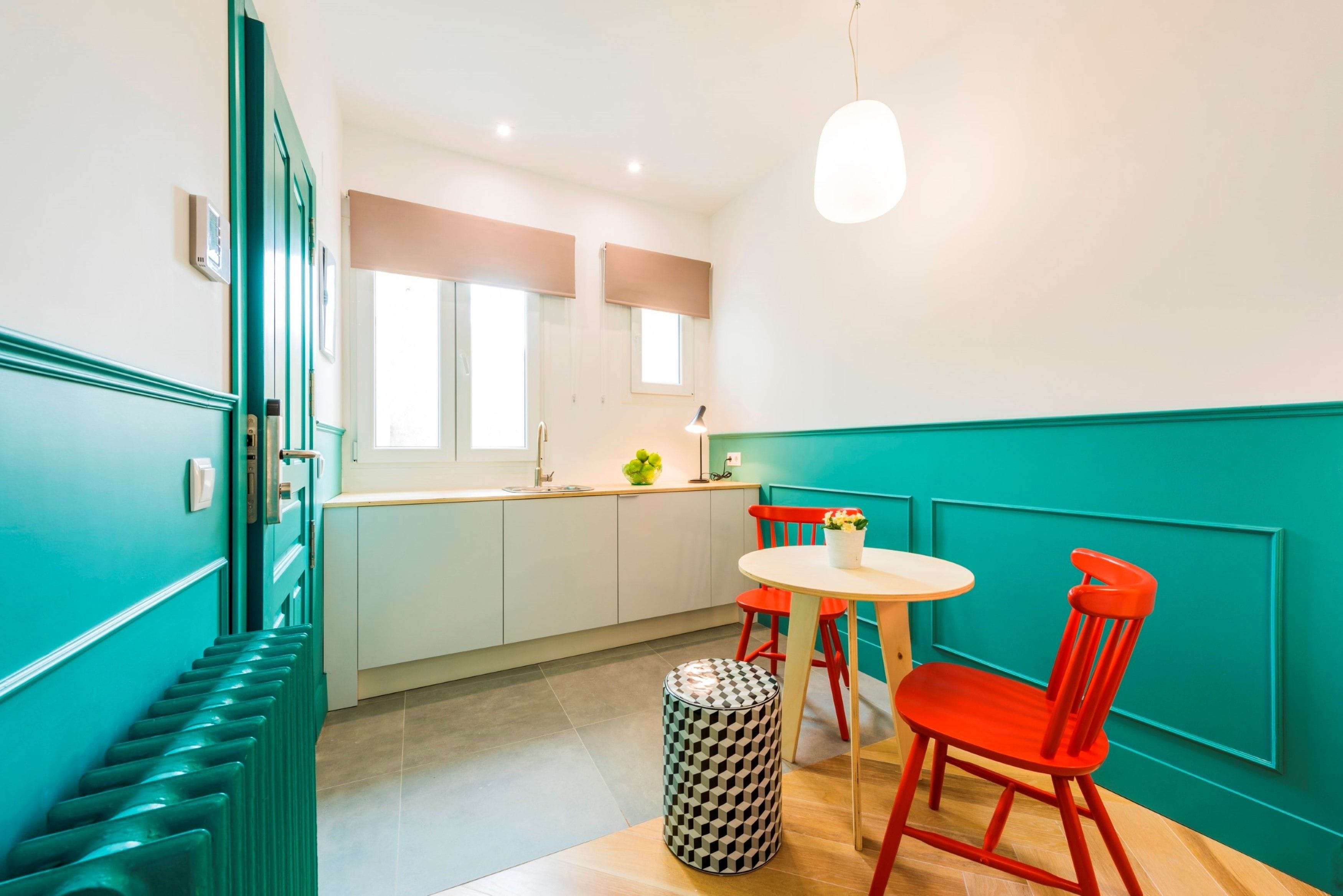 A modern kitchen with teal walls, a white countertop, and red chairs.
