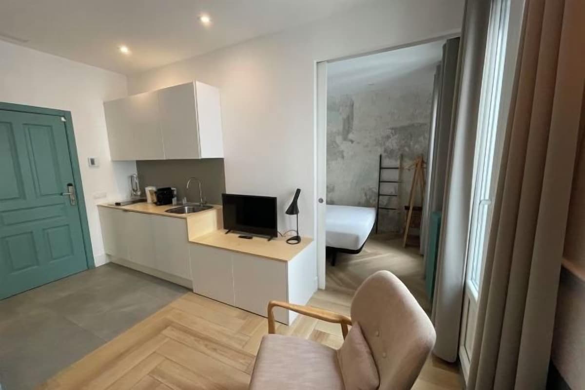 A compact kitchen with white cabinets, a built-in TV, and a small dining area.