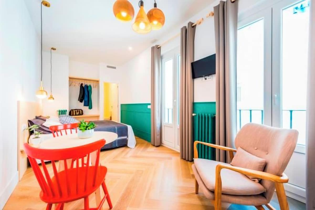 Una sala moderna con un sofá, una mesa de comedor con sillas y un televisor montado en la pared.