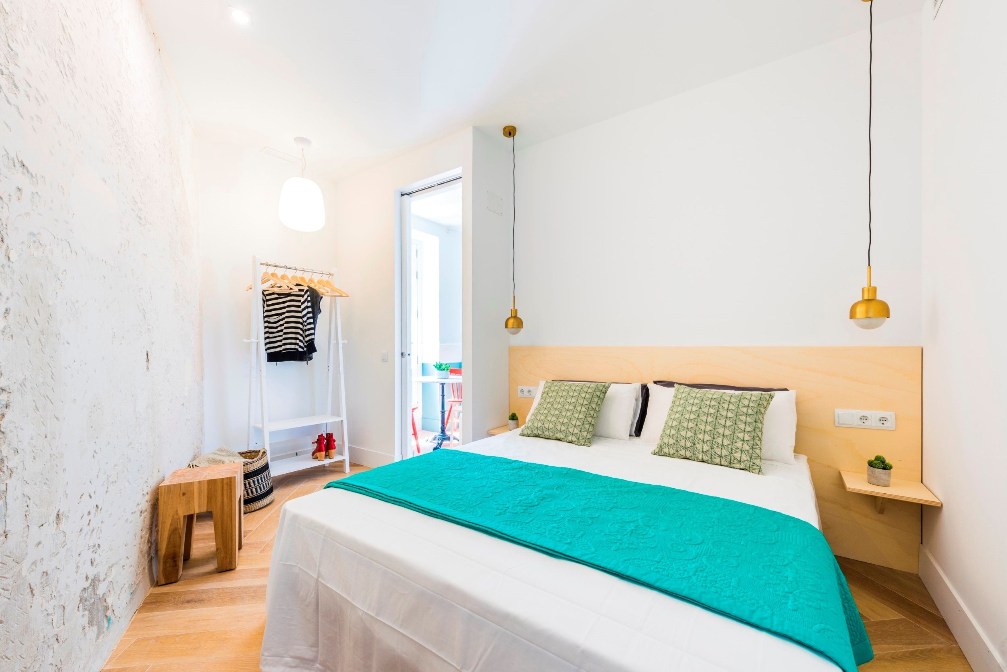 A hotel room with a bed, a wardrobe, a small table, and a hanging light fixture.
