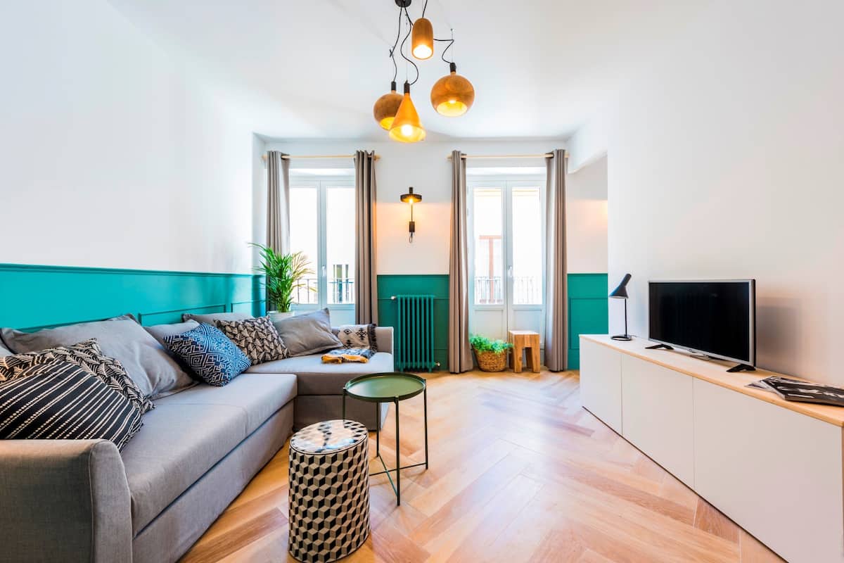 Una sala de estar moderna con un sofá gris, una mesita redonda pequeña, un televisor sobre un mueble bajo y un radiador verde.