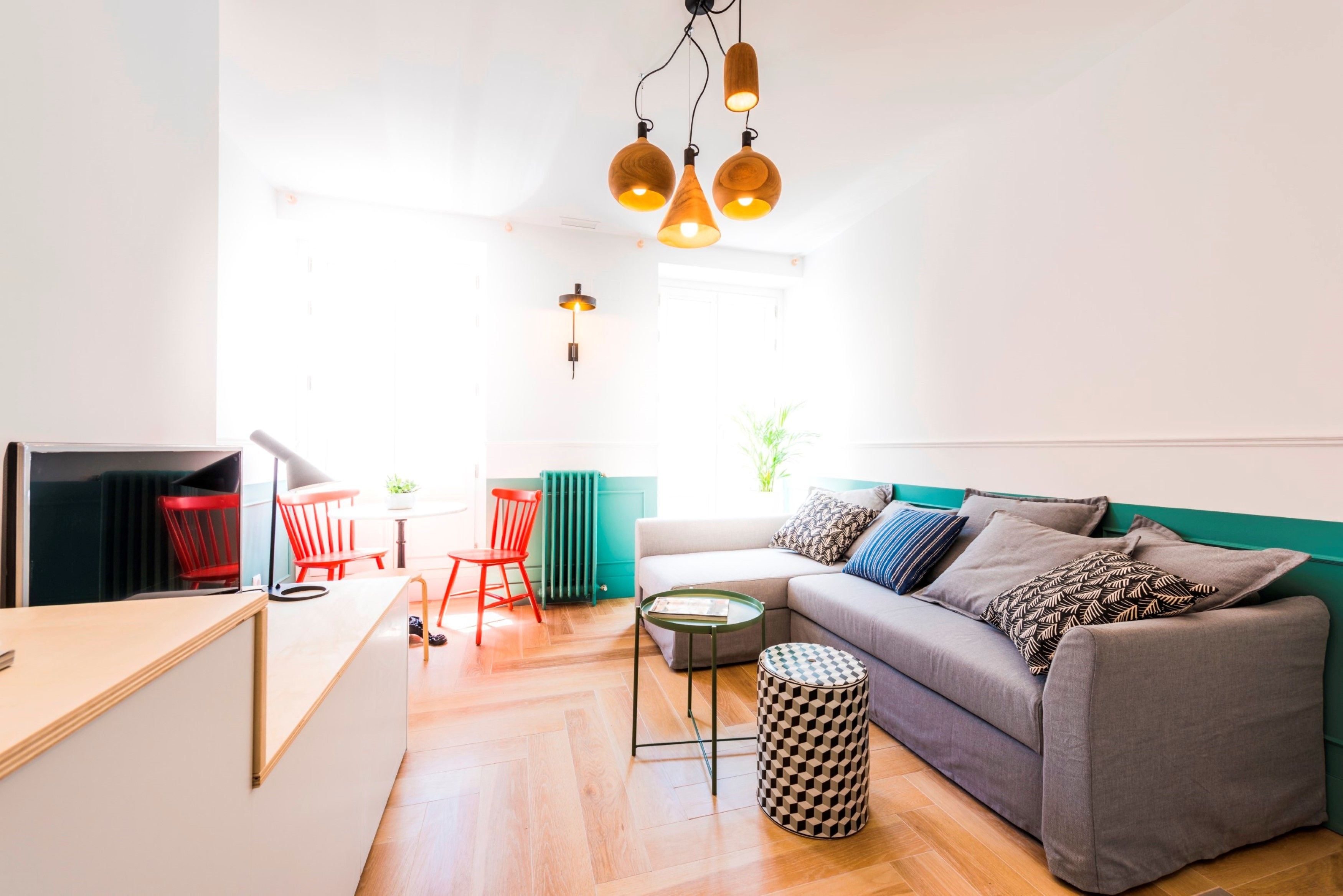 A modern living space with a sofa, a small round table, and a red chair. There is a TV on a stand, a plant, and a window with natural light.