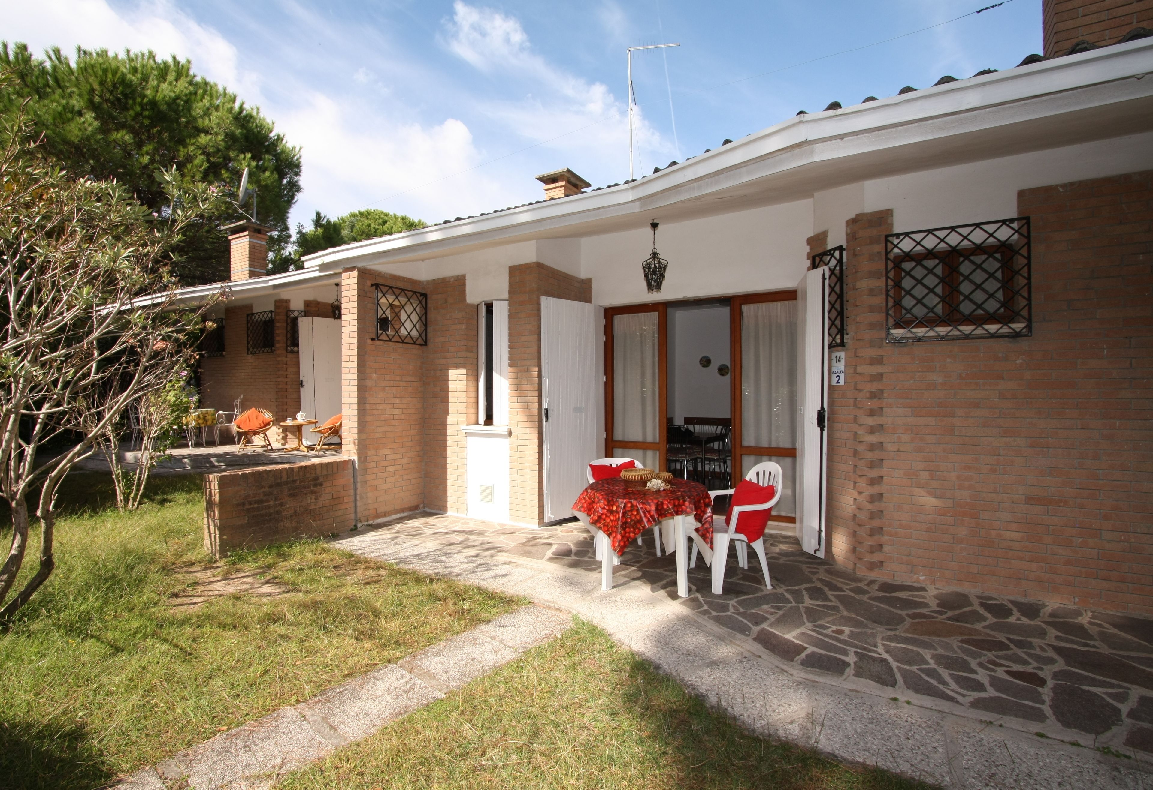 A house with a patio area featuring a table and chairs, a brick exterior, and a door leading to the interior.