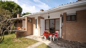 A house with a patio area featuring a table and chairs, a brick exterior, and a door leading to the interior. - Villaggio Azalea (Lignano Sabbiadoro)