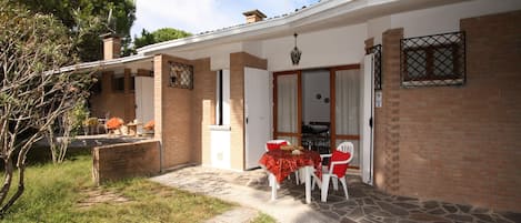 A house with a patio area featuring a table and chairs, a brick exterior, and a door leading to the interior.