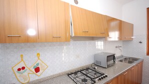 A kitchen with wooden cabinets, a gas stove, a microwave, and a sink. - Villaggio Azalea (Lignano Sabbiadoro)