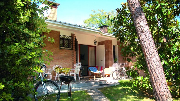A brick house with a porch, a bicycle, and outdoor furniture. - Villaggio Azalea (Lignano Sabbiadoro)