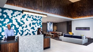 Un área de recepción con una pared de diseño geométrico, un mostrador de recepción, un sofá y un comedor con sillas y una mesa.