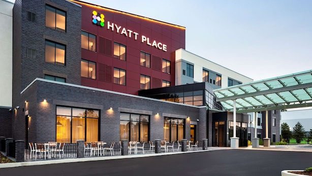 Un hotel moderno con un llamativo letrero de 'Hyatt Place', un área de estar al aire libre y un acceso cubierto.