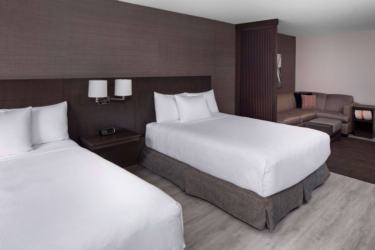 A hotel room with two beds, a sofa, a nightstand, and a lamp.