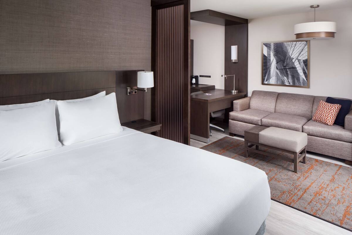 A hotel room with a large bed, a desk, a sofa, and a small table.