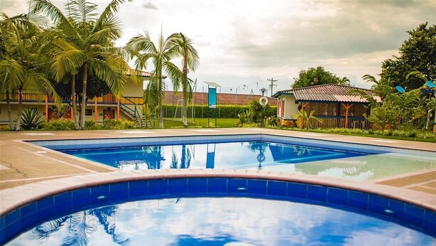 Ein Pool mit geschwungener Kante, umgeben von Palmen und einem Gebäude mit rotem Dach im Hintergrund.