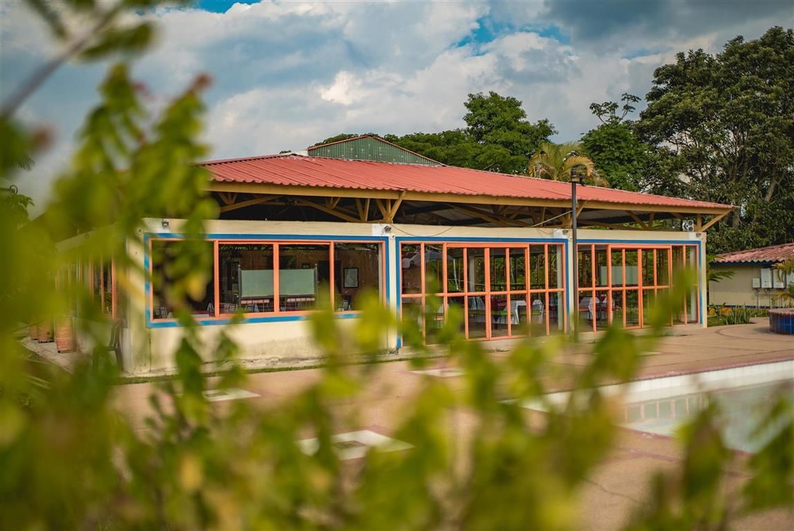 Un edificio con techo rojo y ventanas amplias, rodeado de vegetación.