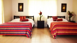 Ein Zimmer mit zwei Betten, jedes mit einer bunten, gestreiften Bettdecke und passenden Kissen. Dazwischen befindet sich ein Nachttisch mit einem Blumenstrauß.