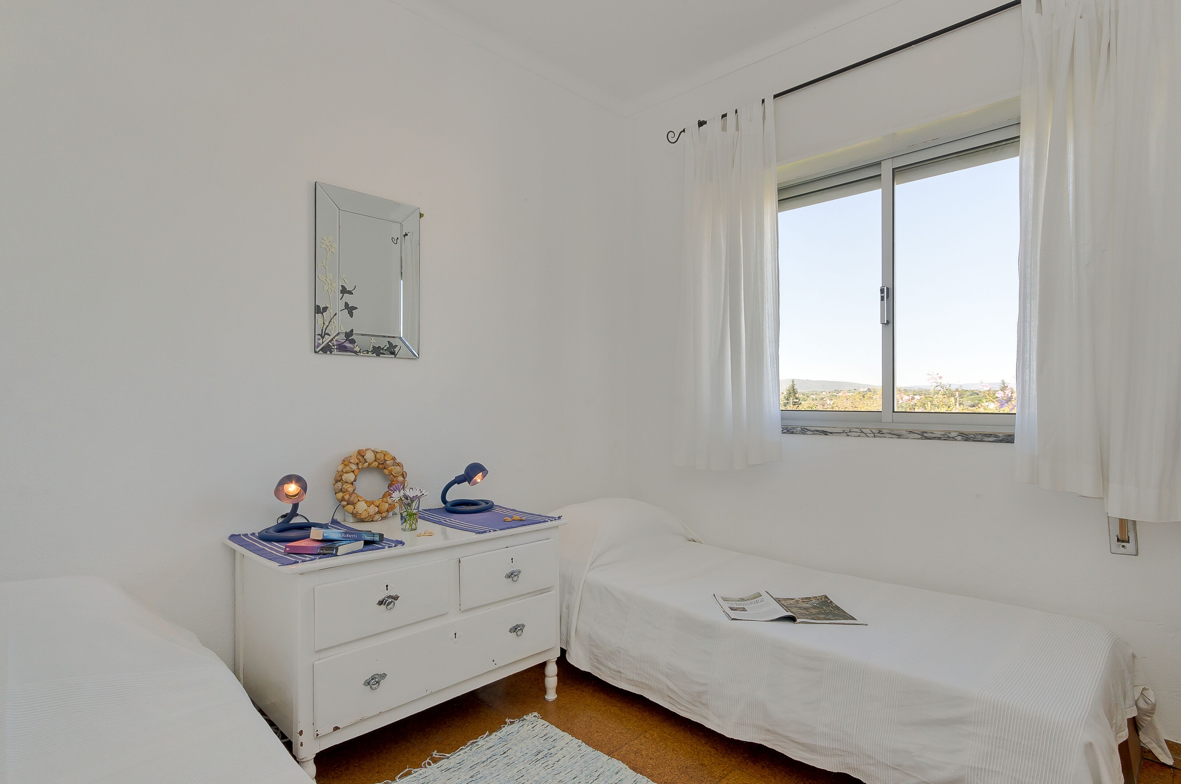 Une chambre à coucher avec un lit, une table de chevet avec une lampe, un miroir et une fenêtre avec des rideaux.