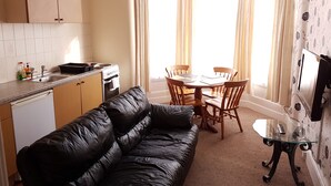 A compact kitchen with a dining area, a black leather sofa, and a small table with a glass top. - Royal Windsor Holiday Apartments (Blackpool)