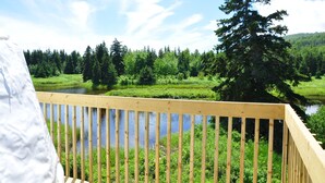 Una terraza de madera con vista a un río tranquilo, rodeada de abundante vegetación y árboles al fondo.