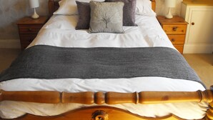 A neatly made bed with a wooden headboard, two bedside tables with lamps, and a nightstand with a vase of flowers. - Historic, homely village retreat with log fires, in stunning Borders. Sleeps 4/6 (Allanton)