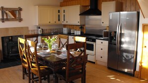 A modern kitchen with wooden cabinets, a stainless steel refrigerator, and a dining table set for four. - Historic, homely village retreat with log fires, in stunning Borders. Sleeps 4/6 (Allanton)