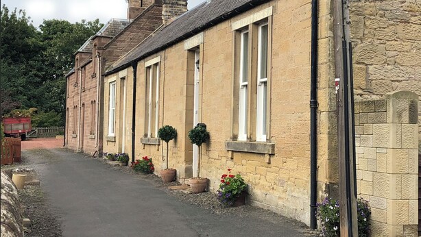A row of stone buildings with large windows and potted plants along the pathway. - Historic, homely village retreat with log fires, in stunning Borders. Sleeps 4/6 (Allanton)