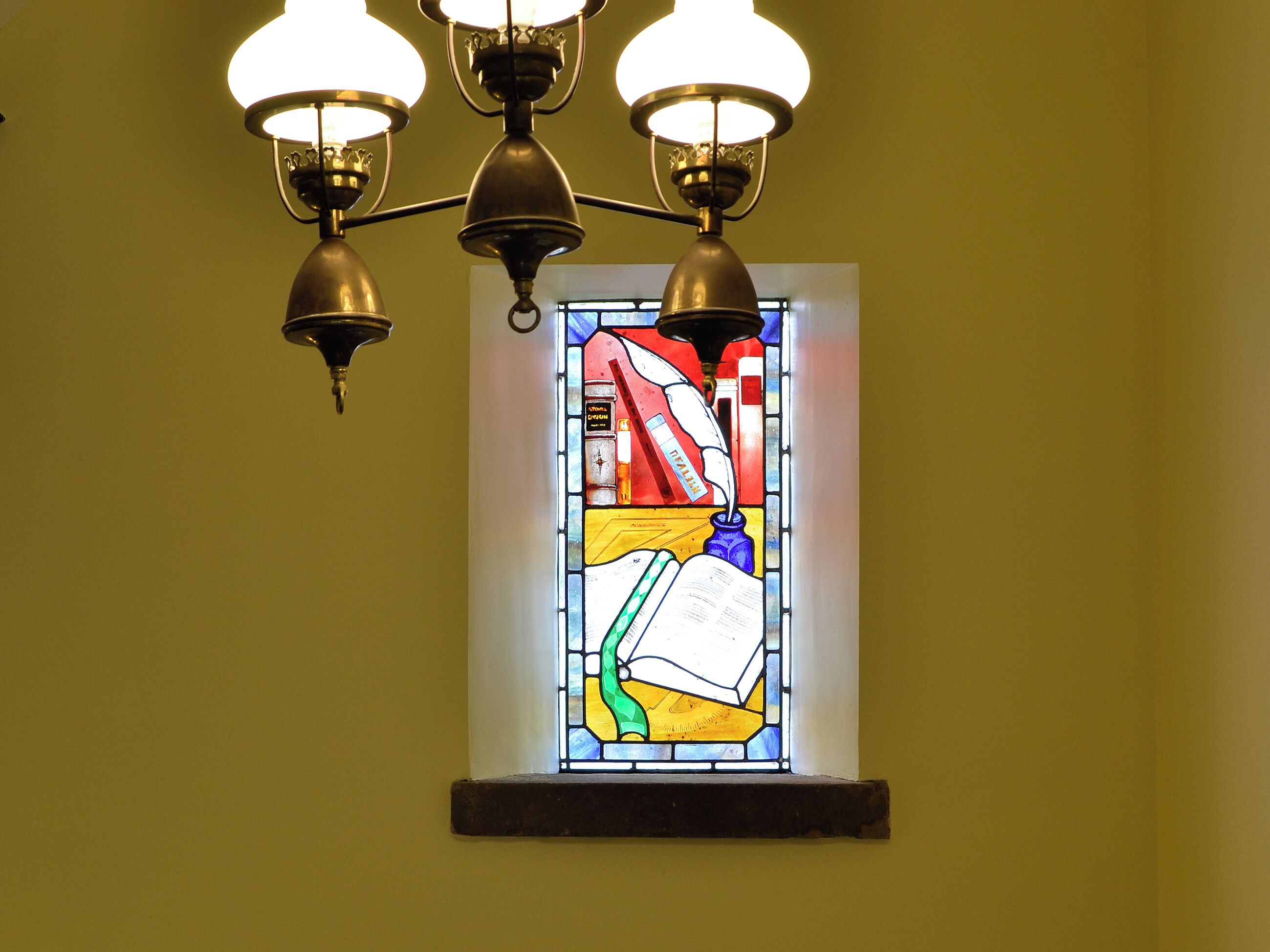 A stained glass window with a book and a candle.